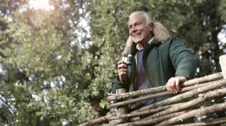 Man in Green Jacket Holding Brown Wooden Fence