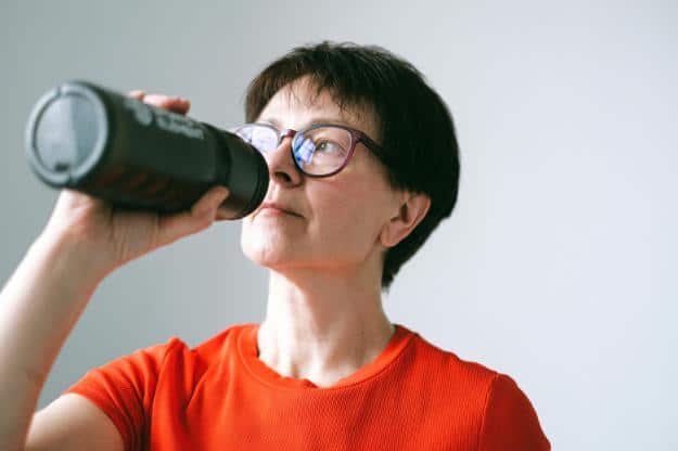 Woman in Orange Shirt Holding and Drinking on Sports Bottle Water | Alzheimer's and Dehydration