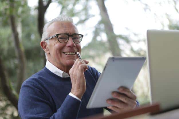 Man in Blue Sweater Holding White Tablet Computer | teach computer skills to seniors px