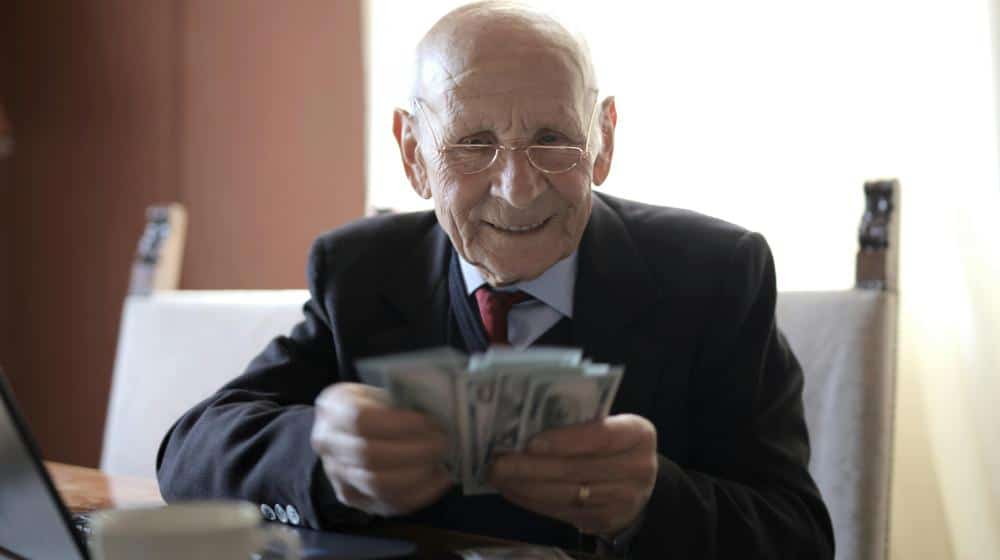 Happy senior businessman counting money while sitting at table with laptop | online banking for seniors px featured image