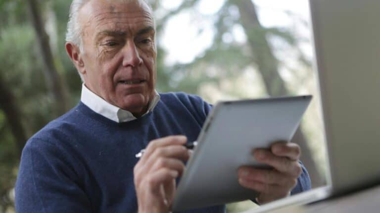 Man in Blue Sweater Holding Silver Ipad | scam prevention for seniors px featured image