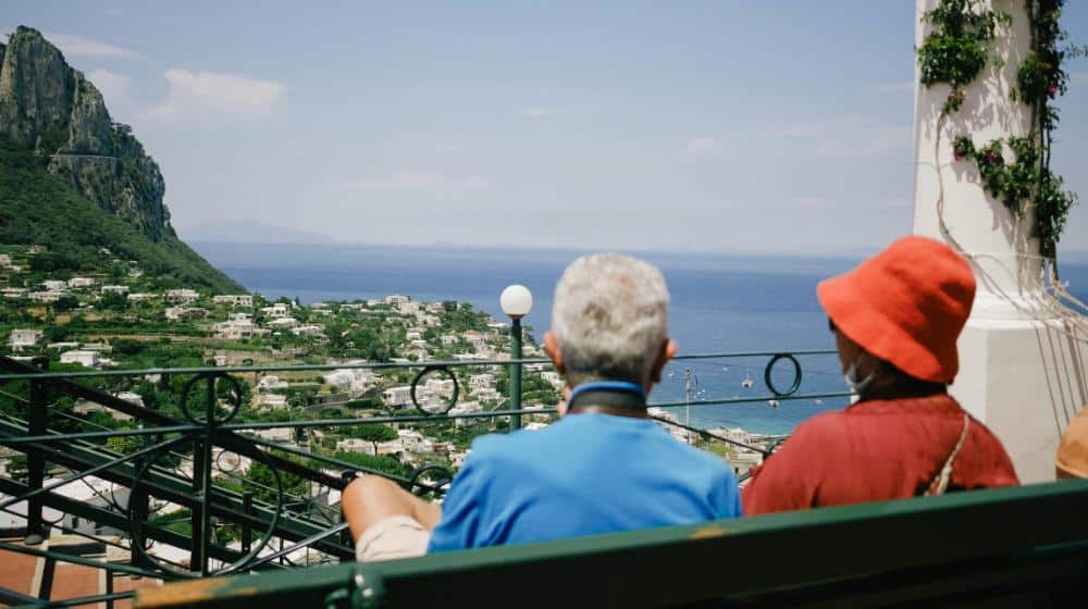 a couple sitting on a balcony overlooking a city and the ocean | senior homelessness us featured image