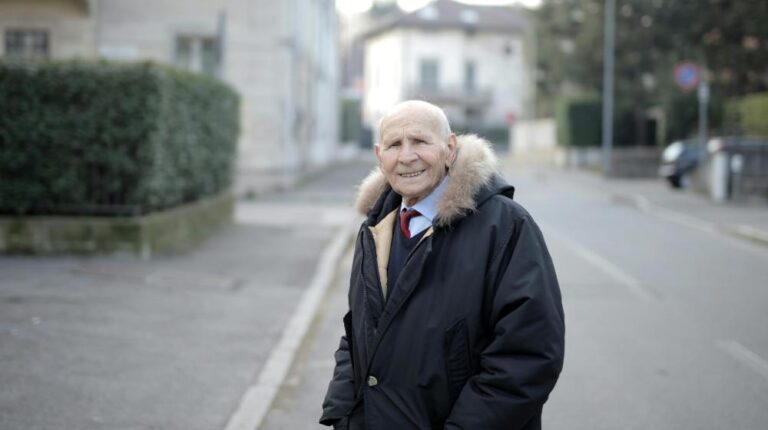 Smiling Man in Black Coat Standing on Sidewalk | Winter Travel Tips for Seniors px featured image